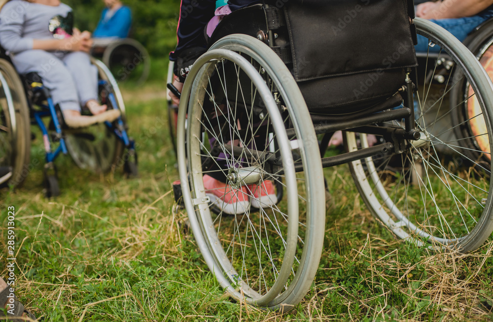 Disabled man resting in a campsite with friends. Wheelchair in the forest on the background of tents Disabled man resting in a campsite with friends. Wheelchair in the forest on the background of tents