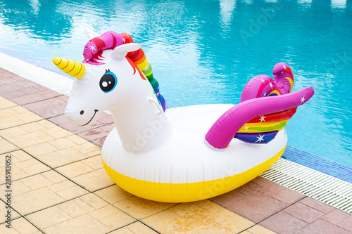 Rainbow coloured inflatable unicorn near swimming pool in the summer, vivid blue water with contrasting white and multicolored unicorn © Marharyta