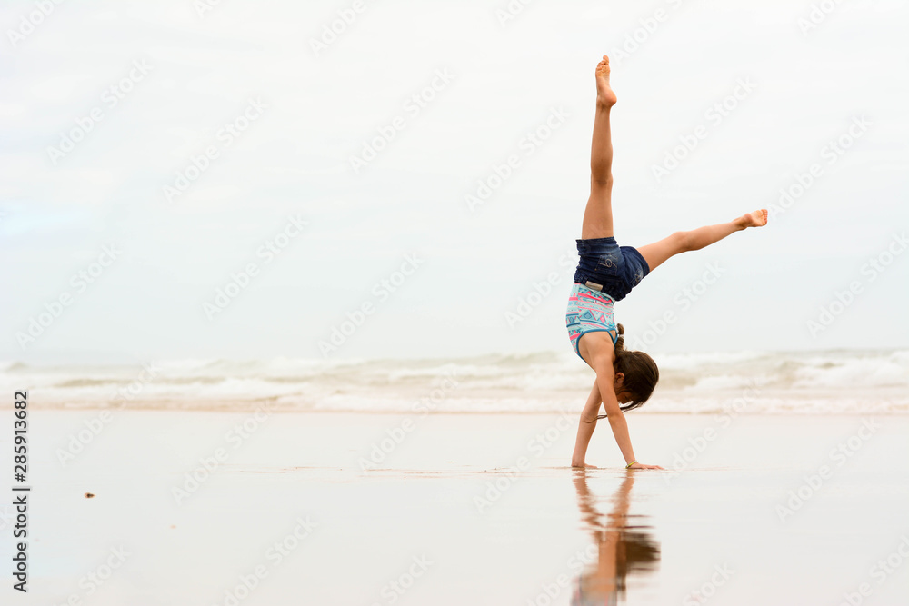 Obraz premium Sport, training, fitness, yoga, active lifestyle concept. Flexible girl gymnast doing acrobatic exercise at the beach.