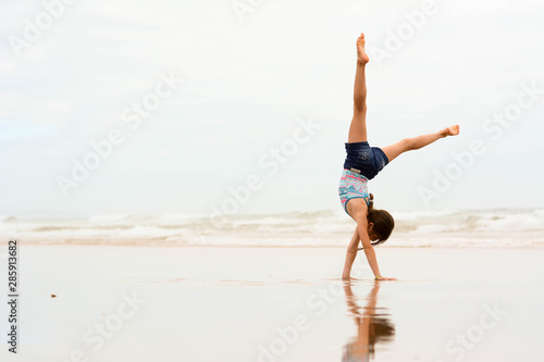 Sport, training, fitness, yoga, active lifestyle concept. Flexible girl gymnast doing acrobatic exercise at the beach.