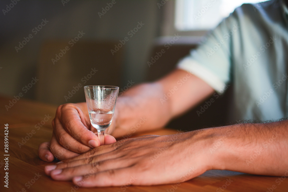 Men's hands hold a crystal glass of alcohol drink on a brighte wooden table at home. Cold alcohol drink served on the table. A man holds a cold alcoholic beverage on a wooden table at home. Men's hands hold a crystal glass of alcohol drink on a brighte wooden table at home. Cold alcohol drink served on the table. A man holds a cold alcoholic beverage on a wooden table at home.