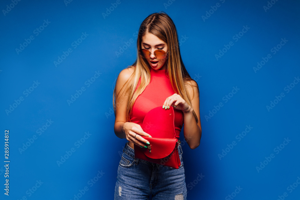 Blonde attractive woman looking an her wallet after shopping on blue background. Blonde attractive woman looking an her wallet after shopping on blue background.