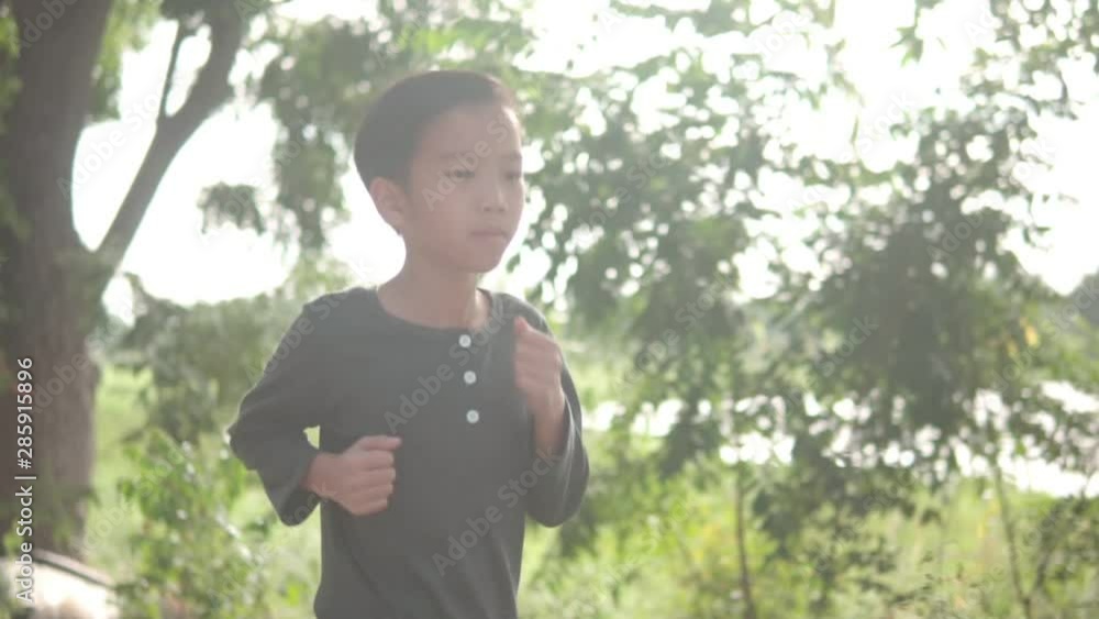 Slow motion camera follow young Asian boy running and lift his arms on a road in the morning in summer day