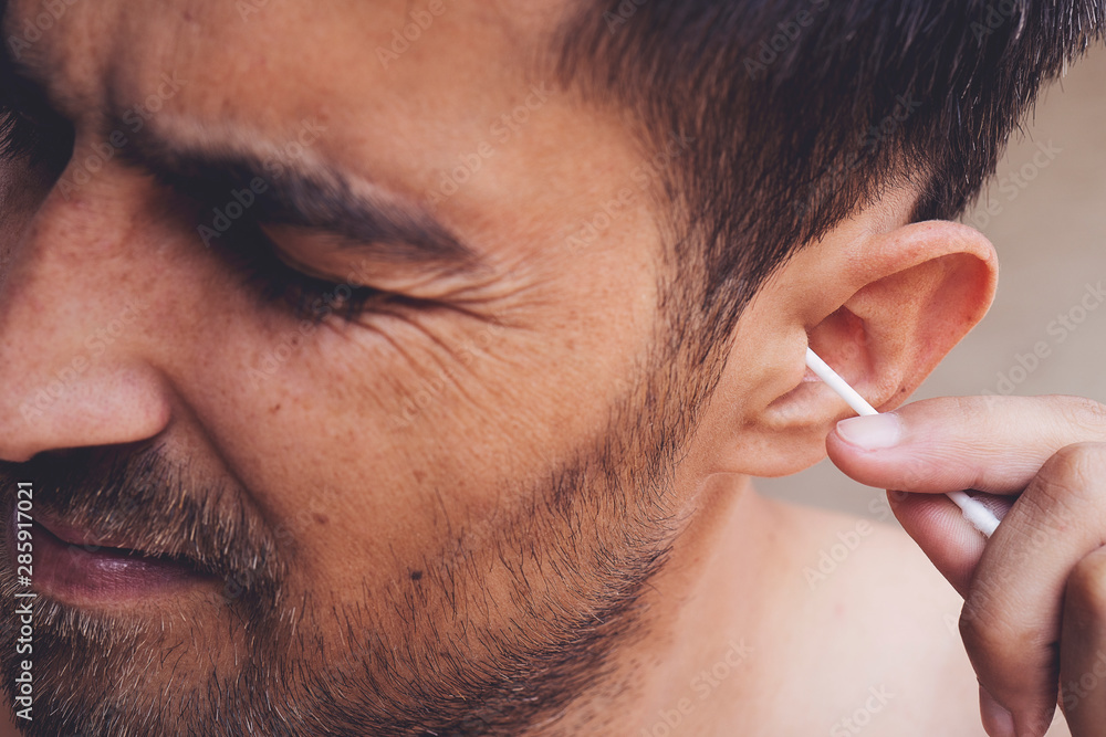 Man about to clean his ears using Q-tip cotton swab. Hygiene essentials  concept. Removing wax from ear. Photos | Adobe Stock