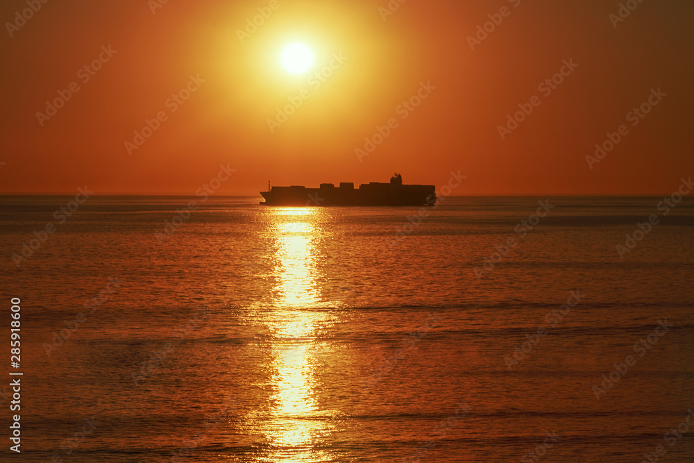 A large vessel on horizon in the atlantic ocean under the bright sun and red sunset.  Sunlight reflection off the water