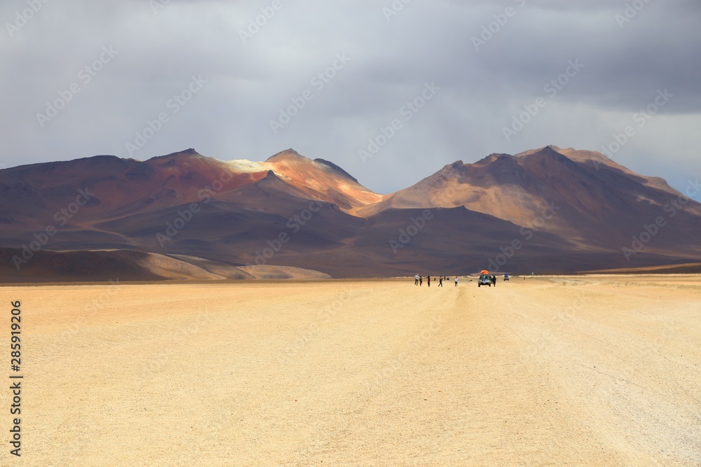 Bolivian desert with arid and dusty soil. Off road adventure in the Andean Highlands. Rally on dusty trails. Cloudy sky and mountains.