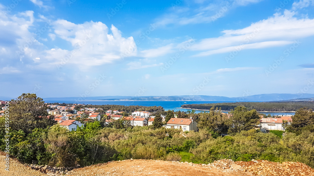 A view on Croatian coastal line from a small hill. Below there is a small city, located directly by the seashore. All the rooftops are dark orange. Sandy beaches in the back.