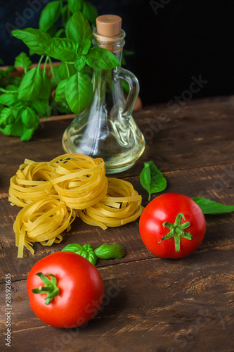 fresh tomatoes basil olive oil glass bottle raw pasta fettuccine on wooden background vertical close up