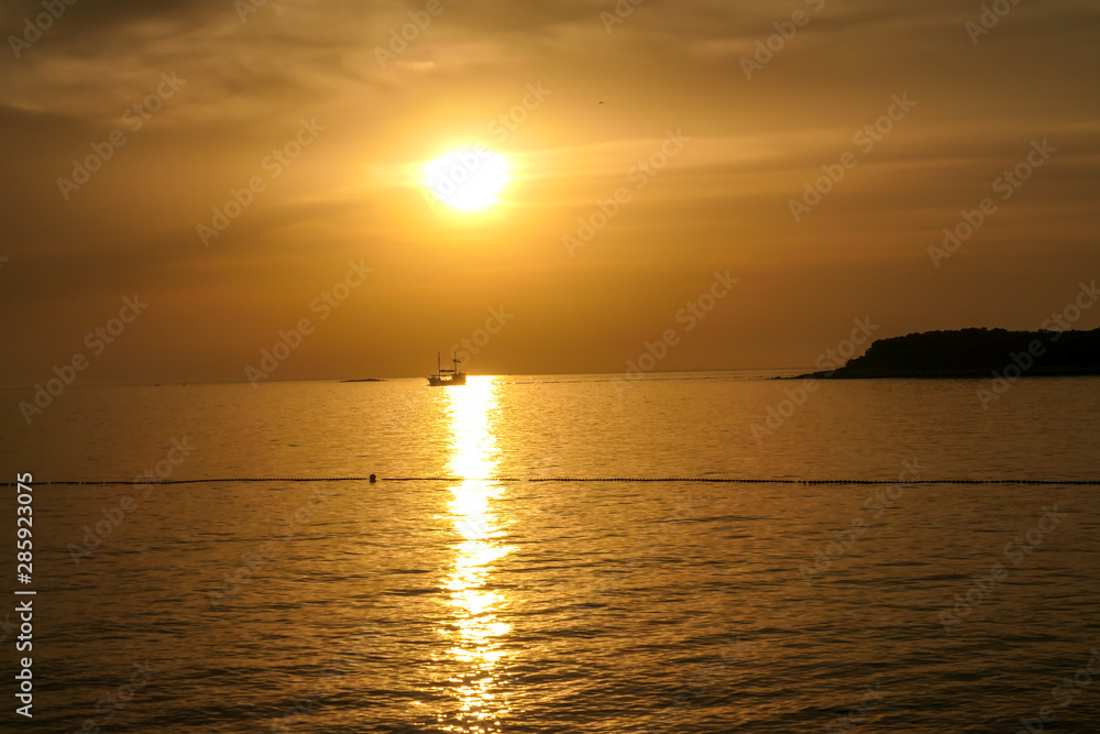Romantic sunset by a beach. The sun sets over the horizon. The sun beams reflecting in the calm sea waters. There is an island on the side. Few birds flying around. The sky turns yellow and orange Romantic sunset by a beach. The sun sets over the horizon. The sun beams reflecting in the calm sea waters. There is an island on the side. Few birds flying around. The sky turns yellow and orange
