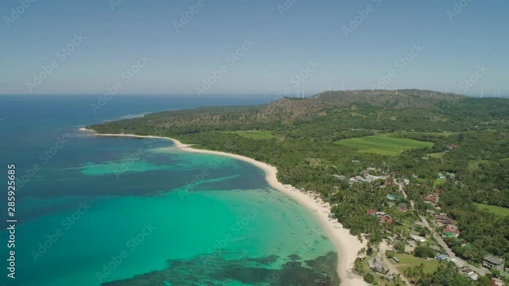 Aerial view of beautiful tropical beach Saud with turquoise water in blue lagoon, windmills. Pagudpud, Philippines. Ocean coastline with sandy beach and palm trees. Tropical landscape in Asia. Aerial view of beautiful tropical beach Saud with turquoise water in blue lagoon, windmills. Pagudpud, Philippines. Ocean coastline with sandy beach and palm trees. Tropical landscape in Asia.