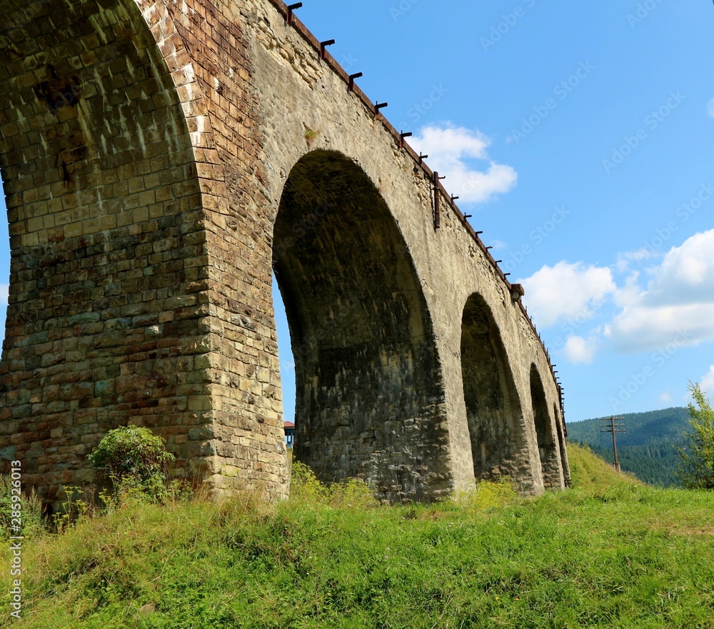  Old viaduct bridge on a background of mountains and green grass