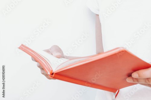 Woman's hands holding pen and red notepad on a white background.  © Christina