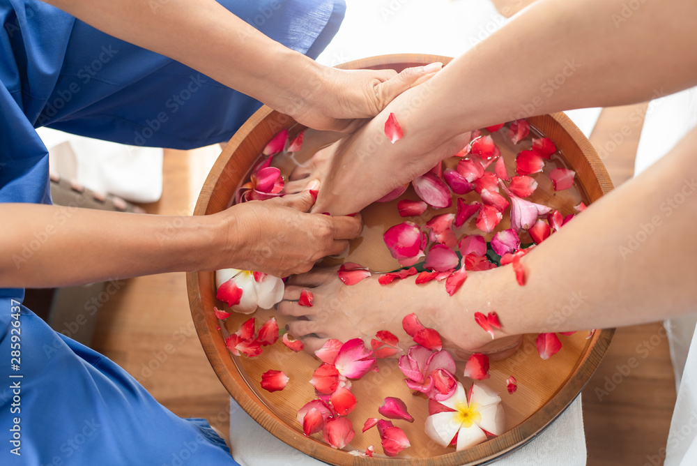 Female feet in wooden bowl with flowers at spa salon Female feet in wooden bowl with flowers at spa salon