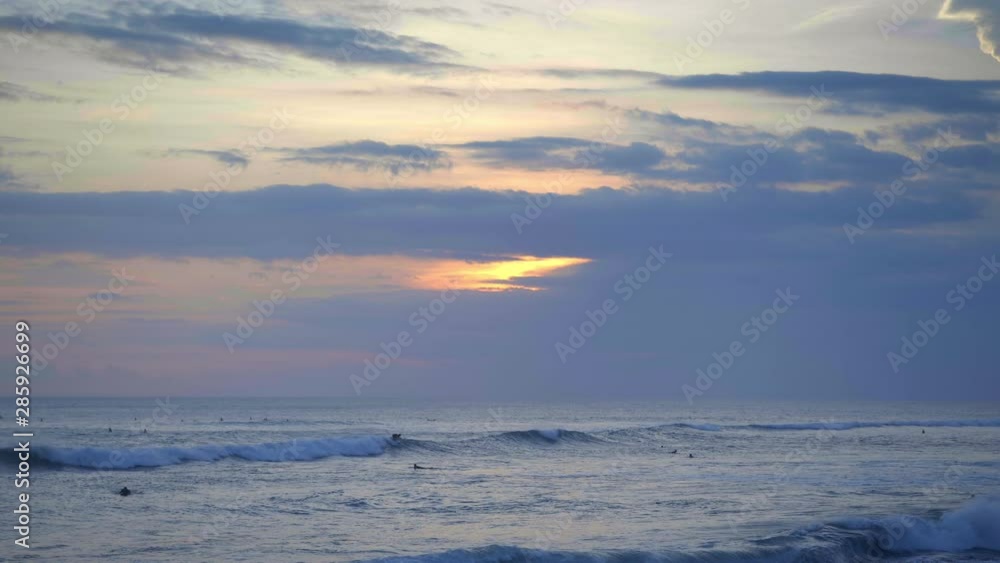 Slow motion of surfers are swimming in warm ocean with big blue waves and foam during beautiful sunset in Bali island Slow motion of surfers are swimming in warm ocean with big blue waves and foam during beautiful sunset in Bali island