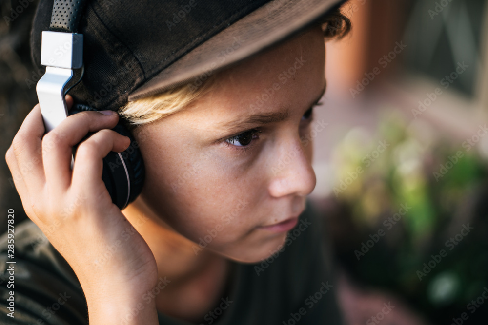 Portrait of a beautiful trendy boy with headphones relax listening music. Close up view of a young male enjoy free time outdoor on a summer evening. Teen enjoying sound. Youth, recreation, fun concept Portrait of a beautiful trendy boy with headphones relax listening music. Close up view of a young male enjoy free time outdoor on a summer evening. Teen enjoying sound. Youth, recreation, fun concept