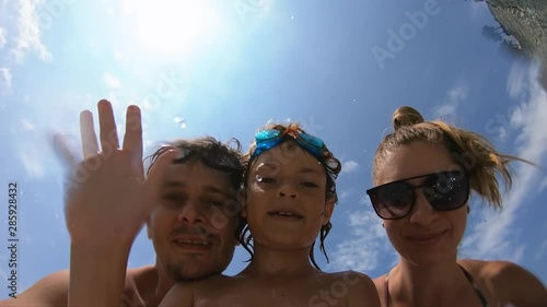 Happy family having fun on sea beach in summer vacation. Smiling, waving hands, grimacing, laughing. View from water. Pov. Healthy, travel, active, childhood, lifestyle concept