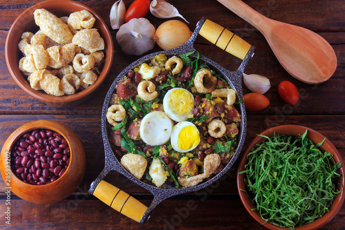 Feijao Tropeiro typical dish of Brazilian cuisine, made with beans, bacon, sausage, collard greens, eggs, on rustic wooden table.