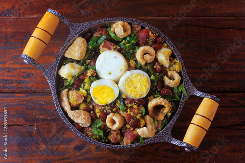 Feijao Tropeiro typical dish of Brazilian cuisine, made with beans, bacon, sausage, collard greens, eggs, on rustic wooden table. photo