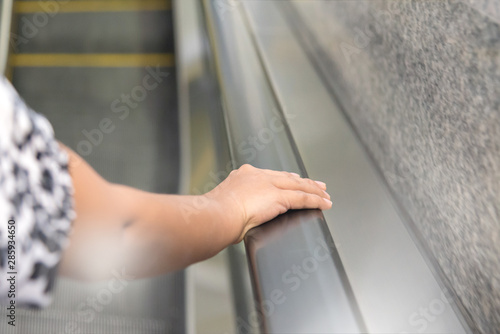 Hands holding the handrail of escalator.