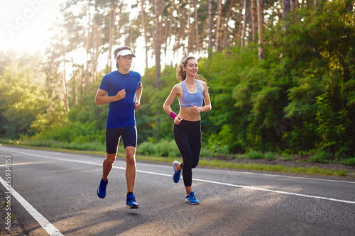 Caucasian female sports woman and fit man in full body length running pine forest road. healthy lifestyle concept