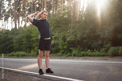 Young curly man warming up at forest road before jogging. Men stretching for running exercises. Handsome 20s athlet doing fitness outdoor © Andrii