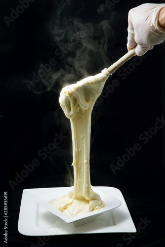 A warm artistic hero shot of fresh hot cheese being served on to a platter with smoke coming off the stretched cheese on a minimal white background from a flat horizontal perspective
