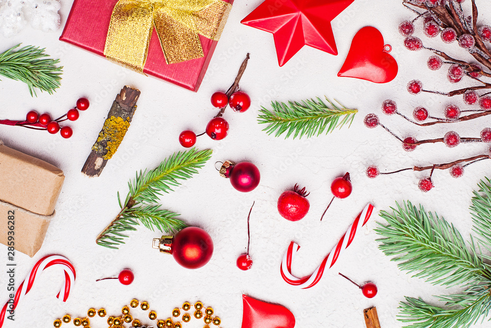 Christmas composition with golden garland, red gift, green Xmas fir branch, red holly berries and baubles on white stucco plaster texture background. Top view flat lay Christmas composition with golden garland, red gift, green Xmas fir branch, red holly berries and baubles on white stucco plaster texture background. Top view flat lay