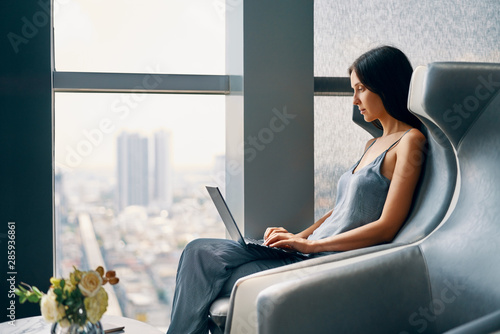 Young woman working on laptop while sitting in a big comfortable chair at modern interior photo