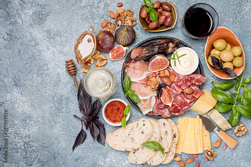 Italian antipasti wine snacks set. Cheese variety, nuts, Mediterranean olives, sauces, Prosciutto di Parma or jamon, and wine over gray background, top view photo