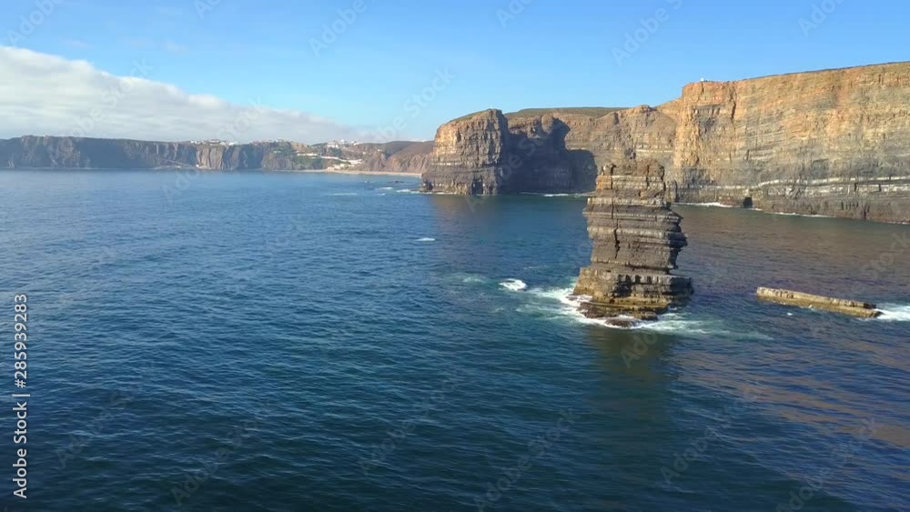 Aerial, tracking, drone shot, of a huge rock, in the water, on the Atlantic sea, near Pedra da Agulha, Arrifana Beach, in the background, on a sunny day, in Vicentina coast national park, in Portugal Aerial, tracking, drone shot, of a huge rock, in the water, on the Atlantic sea, near Pedra da Agulha, Arrifana Beach, in the background, on a sunny day, in Vicentina coast national park, in Portugal