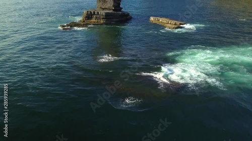 Aerial, tilt up, drone shot, over the sea, revealing a big rock, on the Atlantic ocean, near Pedra da Agulha, towards Arrifana Beach, on a sunny day, in Vicentina coast national park, in Portugal
