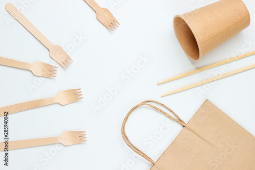 Disposable tablewar of natural materials. Eco friendly concept. Wooden forks, empty craft coffee cup, bag, chopsticks on a white background. Top view photo