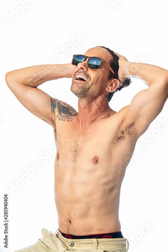 Healthy, shirless, muscular, middle aged man smiling while feeling handsome wearing reflective leaopard print sunglasses in high key background.