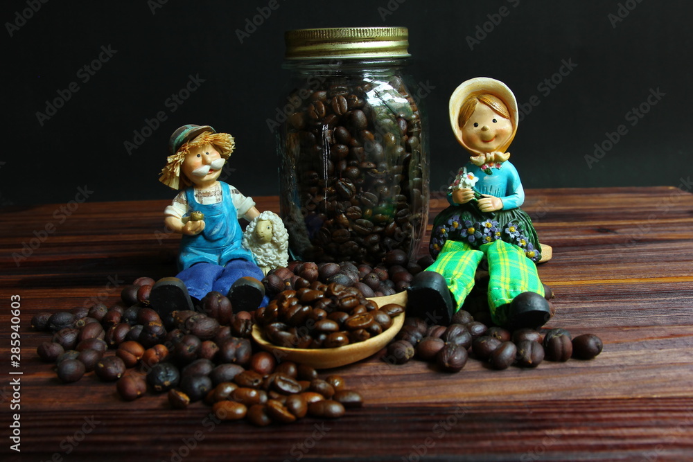 farmer dolls sit on coffee beans.dried coffee beans with roasted coffee beans .coffee beans on wood spoon on brown wood floor .