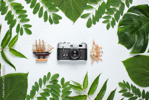 Retro style travel still life. Film camera, shells, green tropical leaves. Traveler accessories on a white background. Top view photo