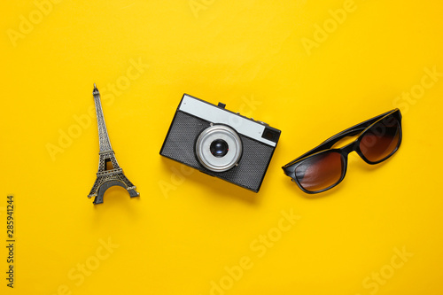 Jorney to Paris. Sunglasses, retro camera, figurine of the Eiffel tower on yellow background. Travel background. Top view