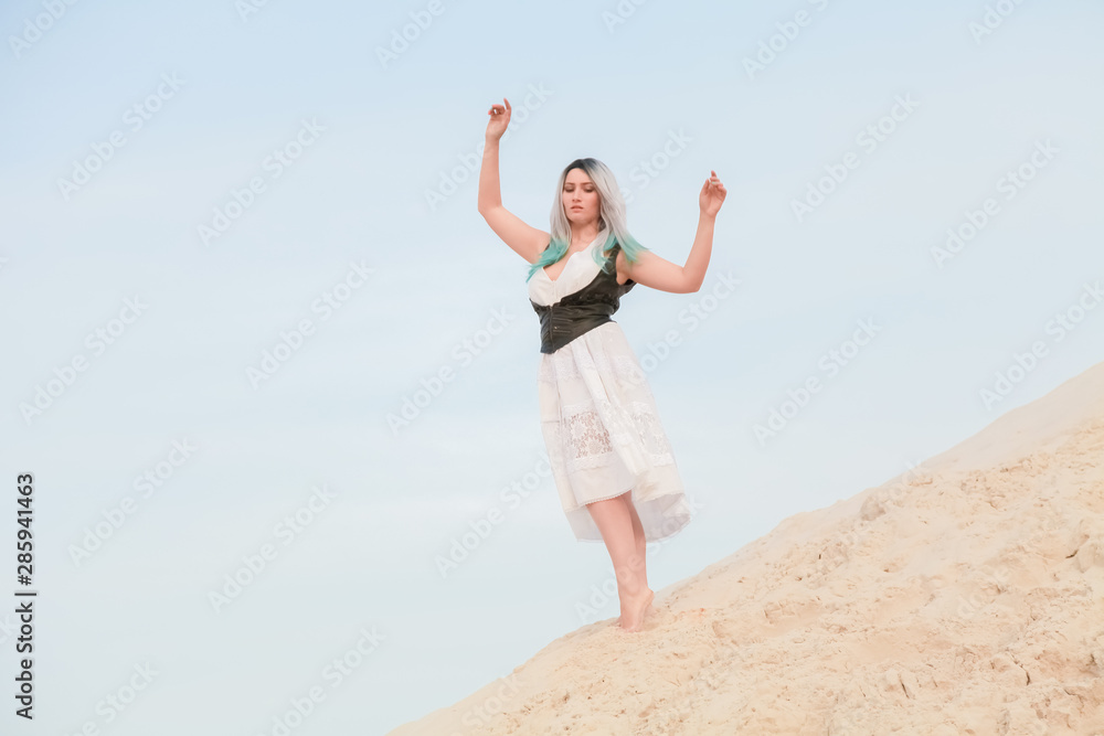Young beautiful Caucasian woman in white dress and brown leather waistcoat posing in desert landscape with sand. Young beautiful Caucasian woman in white dress and brown leather waistcoat posing in desert landscape with sand.