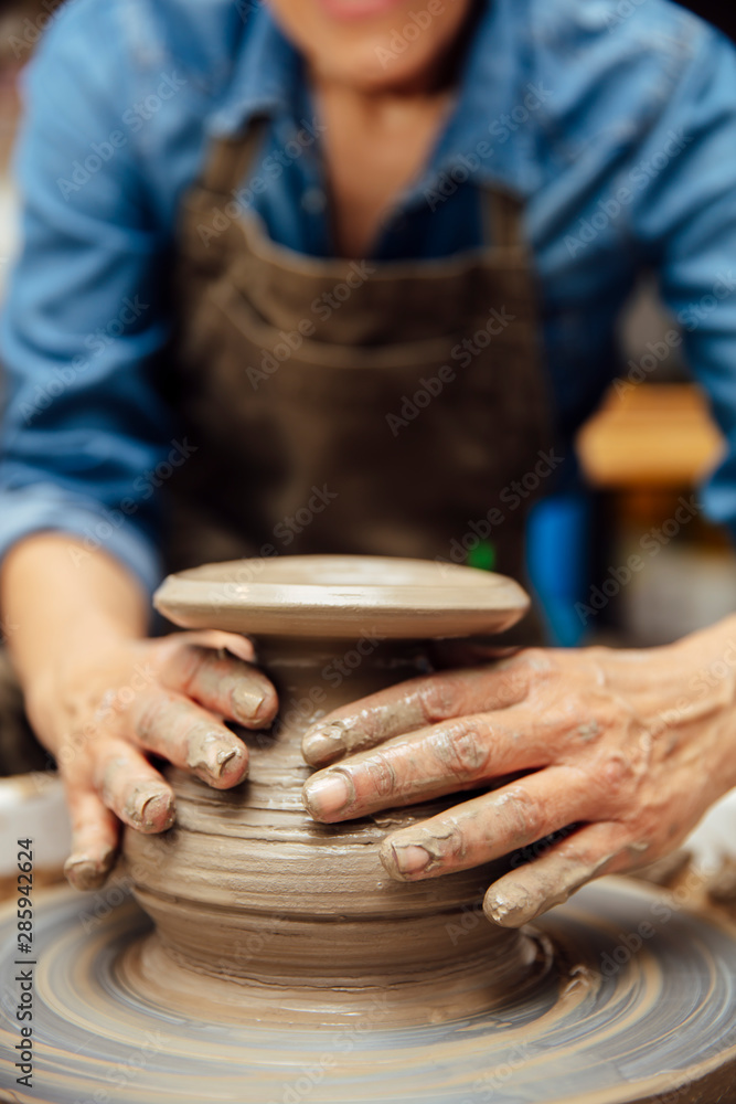 Senior female potter working on pottery wheel while sitting in her workshop Senior female potter working on pottery wheel while sitting in her workshop