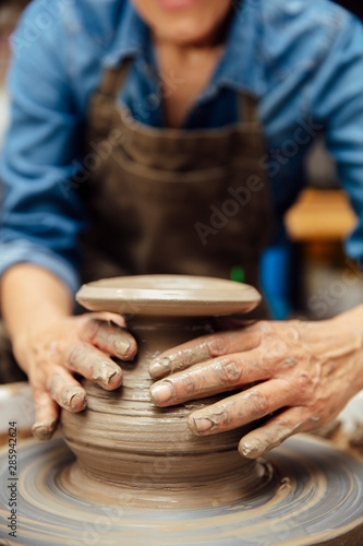 Senior female potter working on pottery wheel while sitting  in her workshop