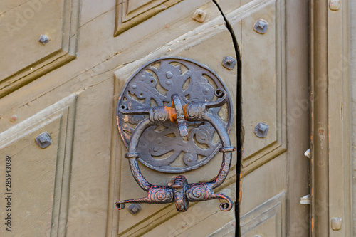 Antique brass door knocker in the shape, door element with metal knob. A very old door handle and lock on a vintage wooden building.