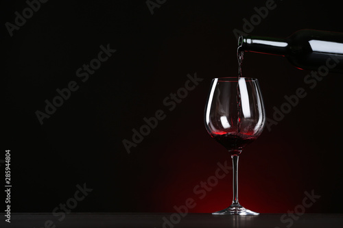 Pouring wine from bottle into glass on table against dark background, space for text