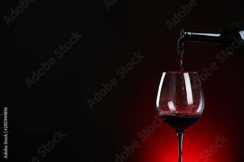 Pouring wine from bottle into glass on dark background, space for text