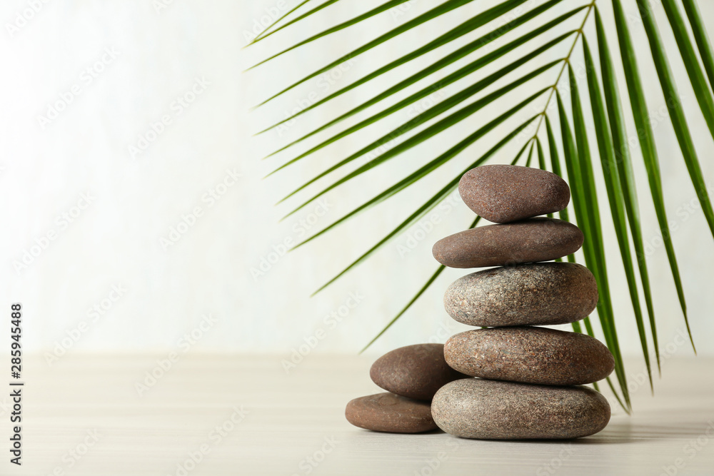 Stack of spa stones and palm leaf on table against white background, space for text - obrazy, fototapety, plakaty 