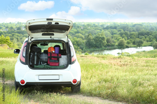 Car with camping equipment in trunk on green field. Space for text