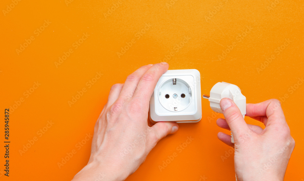 Female hands plug in power plug into electro outlet on orange background. Minimalism. Top view - obrazy, fototapety, plakaty 