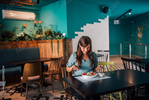 Young smiling woman eating delicious healthy food at restaurant.