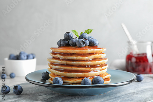 Plate of delicious pancakes with fresh blueberries and syrup on grey table against light background photo