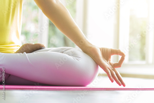 Young sporty woman practicing yoga lesson sitting in Sukhasana exercise, Easy Seat pose with mudra gesture, working out, female arms with wrist bracelets close up