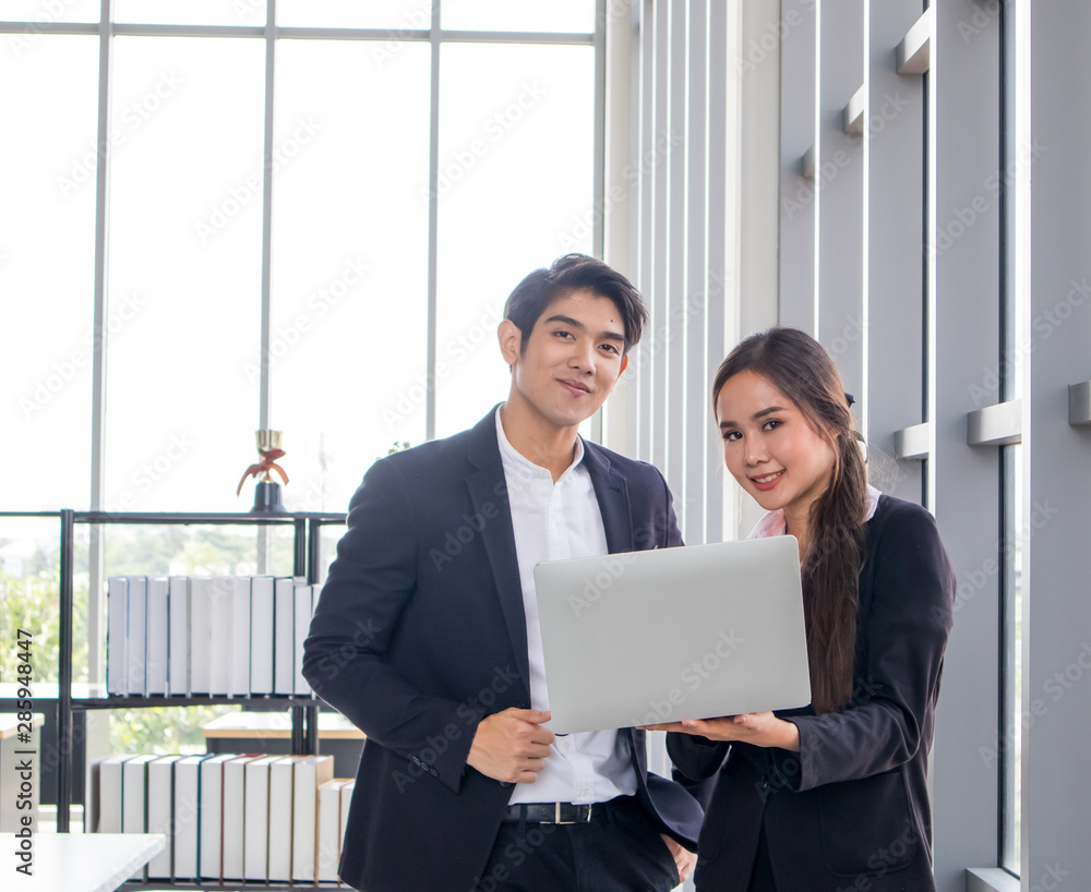 Young Asian businessmen and business women consult the work together. By looking at the notebook in the workplace Young Asian businessmen and business women consult the work together. By looking at the notebook in the workplace