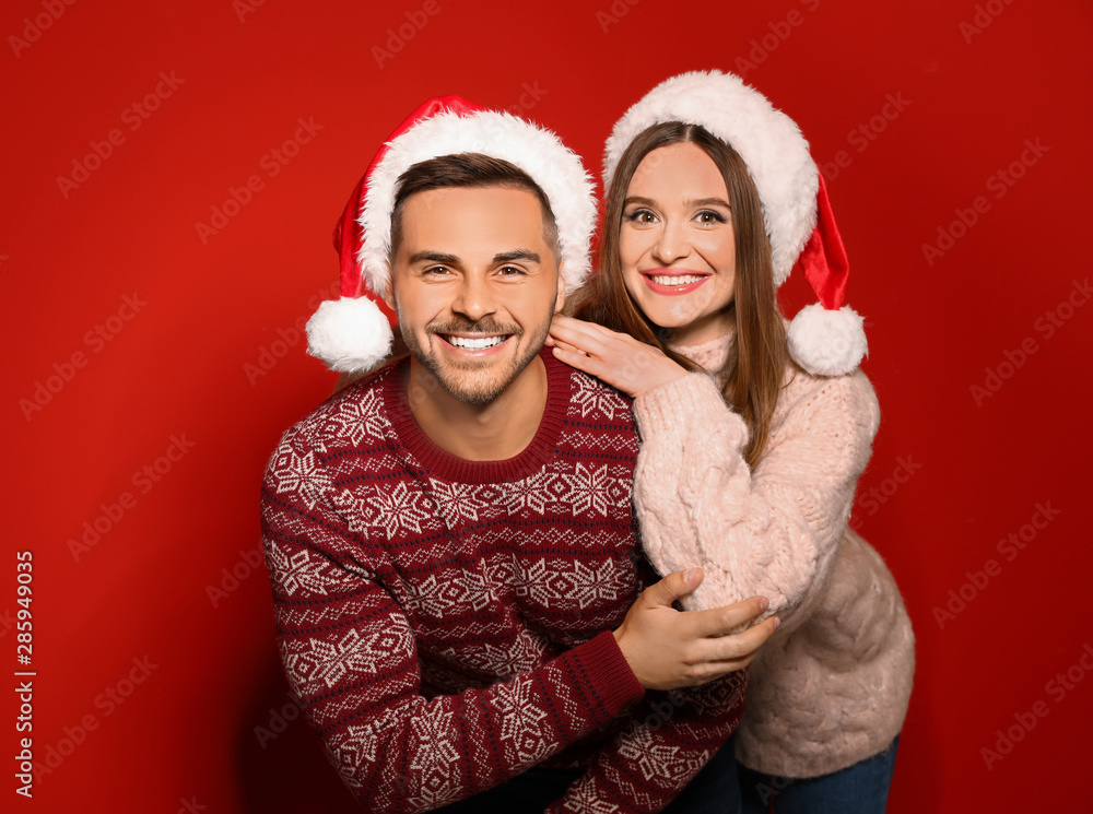 Couple wearing Christmas sweaters and Santa hats on red background Couple wearing Christmas sweaters and Santa hats on red background